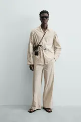 Camisa de calce relajado con diseño de rayas verticales, cuello bowling y manga larga. Cuenta con cierre frontal de botones y tres bolsillos de plastrón: uno en el pecho y dos en la cadera.