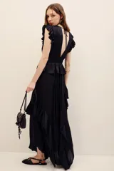 Vestido largo negro de poliéster, con escote en V profundo, mangas sisa con volados en los hombros, cintura elastizada con diseño fruncido y falda larga con capas y volados.