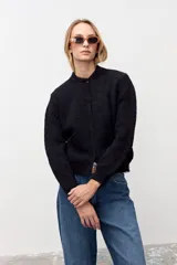 Cardigan negro de tejido de punto con sutiles destellos brillantes, cuello redondo, cierre frontal con botones y mangas largas con puños acanalados.