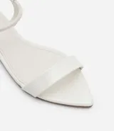 Sandalias planas blancas con tira elástica en el tobillo y tira fija sobre los dedos.