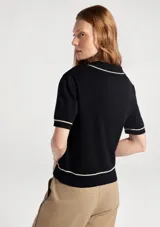 Polo de manga corta en tejido de punto color beige, con cuello tipo polo y detalles de líneas finas en color negro en el cuello, mangas y ruedo.