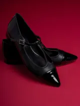 Chatitas negras de cuero sintético con punta charol y tira con hebilla.
