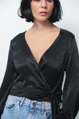 Camisa tipo blusa cruzada de seda negra, con escote en V profundo, mangas largas con puños abotonados y lazo lateral para anudar en la cintura.