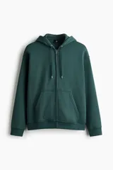 Campera con capucha de felpa de peso medio con interior cepillado suave. Presenta hombros caídos, cierre frontal, bolsillos tipo canguro y cordones ajustables en la capucha. Los puños y el bajo están terminados en punto acanalado.