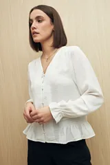 Camisa negra de manga larga con escote en V y botones forrados al tono en el frente. Destaca por su textura sutil y por el detalle de frunces con volados en la parte inferior.