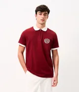 Chomba bordó de manga corta con cuello polo y cierre frontal. Cuenta con cuello y puños en color blanco, y un escudo bordado en el pecho. Confeccionada por la marca Marfinno en mezcla de algodón y poliéster.