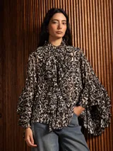 Blusa de gasa con estampado ikat en tonos blanco y negro, con cuello alto, volados frontales tipo jabot y mangas largas con volados en los puños.