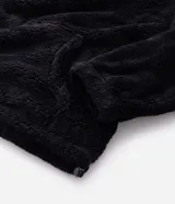 Buzo de felpa sintética tipo corderito negro con cuello alto, cierre frontal parcial, bolsillo tipo canguro y etiqueta aplicada en el pecho.