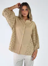 Camisa de algodón color beige, de corte holgado y mangas largas abullonadas con diseño de broderie en mangas y laterales, cierre frontal de botones y cuello camisero.
