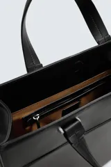 Bolso de hombro liso color negro, con cierre de imán en el compartimento principal y bolsillo interior con cremallera. Incluye un charm decorativo, dos asas de mano y un asa de hombro ajustable y extraíble.