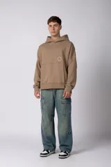 Buzo canguro oversize de frisa de algodón premium en color azul grisáceo. Presenta un diseño con recortes frontales, bolsillo tipo canguro y un pequeño logo circular estampado en el pecho. Cuenta con puños y ruedo acanalados.