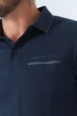 Polo de manga larga negra con cuello clásico, tapeta de dos botones y bolsillo de parche en el pecho con ribete blanco. Logo de la marca bordado en blanco sobre el bolsillo.