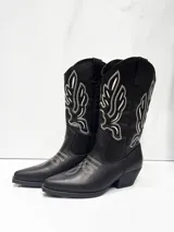 Botas estilo cowboy de caña media en color marrón oscuro, con punta fina y taco cuadrado. Presentan costuras decorativas en contraste de color blanco en la caña y el empeine.
