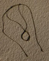 Collar artesanal con dije de metal irregular en forma de aro orgánico, montado sobre un cordón de algodón natural ajustable.