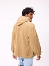 Canguro de pana color tostado con capucha, cordones ajustables, cierre frontal parcial con botones y dos bolsillos delanteros. Presenta puños elásticos y un diseño de calce relajado.