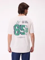 Remera de corte holgado color crema con estampado gráfico en la espalda que incluye el número 85, personajes animados y la frase Play Hard, Surf Harder.