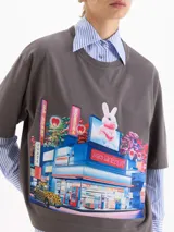 Remera de algodón color gris con estampa gráfica frontal de estilo anime que representa un mercado con un conejo. Presenta un corte amplio, cuello redondo y mangas cortas.