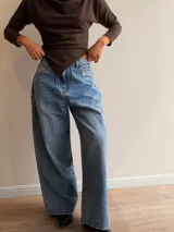 Pantalón de jean estilo palazzo en tono celeste medio, con corte amplio y recto. Presenta detalles de roturas sutiles en los bolsillos y ruedo, con cierre frontal y bolsillos laterales.