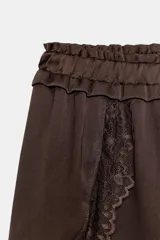 Shorts de tiro bajo confeccionados en satén color marrón, con cintura elástica y detalles de encaje a tono en los laterales y el ruedo.