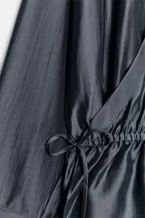 Blusa fluida cruzada de diseño envolvente, color gris oscuro satinado, con mangas largas y puños anchos. Cuenta con cuello mao y cordón ajustable en la cintura con lazada lateral.