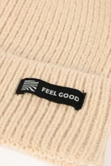 Gorro beanie tejido de punto grueso en color beige, con vuelta y pequeña etiqueta decorativa negra con la inscripción 'FEEL GOOD'.