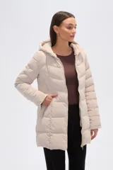 Campera acolchada color beige claro, de largo medio, con capucha y cierre frontal. Presenta costuras horizontales y diagonales que crean un efecto matelassé.