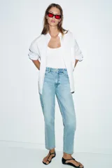 Jeans de denim azul claro lavado, tiro alto, corte Mom Fit con pierna recta y largo tobillero. Presenta cinco bolsillos y cierre frontal con cremallera y botón.