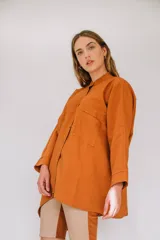 Camisa de sarga color mostaza, de diseño irregular con los costados más largos, mangas largas y corte amplio.