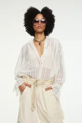 Blusa oversize blanca de encaje calado semitransparente, con cuello mao, cierre frontal de botones, mangas largas abullonadas con puños fruncidos y aberturas laterales en el ruedo.