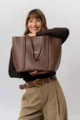 Bolso tipo tote de color marrón, confeccionado en material símil cuero texturado. Presenta un diseño estructurado con asas largas para llevar al hombro y el logo de la marca aplicado en la parte frontal.