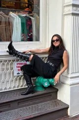 Botas altas de cuero negro con acabado brillante texturado, múltiples tiras con hebillas y tachas plateadas, cordones frontales, punta fina y taco bajo escultural.