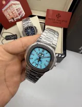 Reloj Patek Philippe modelo 5712 con movimiento automático, cristal de zafiro, malla de acero inoxidable y sumergible. Presenta una esfera turquesa con indicadores de día, fecha y fase lunar.