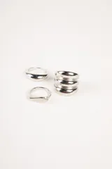 Set de anillos plateados con diferentes diseños: uno liso y grueso, otro con forma de sello y un tercero con varios anillos finos unidos.