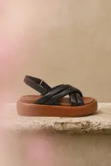 Sandalias de plataforma con capellada de tiras cruzadas acolchadas de cuero color negro, base marrón de goma EVA y tira trasera con ajuste mediante hebilla metálica.