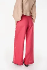 Pantalón de lino blanco de corte ancho y fluido, con cintura alta que incorpora una sobrepretina ancha desmontable con pliegues horizontales.