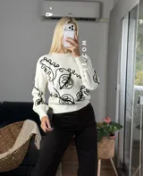 Sweater de tejido de punto con cuello redondo y diseño de bordado lineal en contraste que forma motivos orgánicos y florales. Presenta un corte clásico y mangas largas.