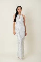 Vestido largo de fiesta en gasa labrada color blanco con detalles plateados, con cuello halter, drapeado en la cintura y tajo en la parte trasera.