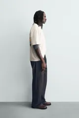 Camiseta de corte relajado color crudo, con cuello redondo y manga corta. Presenta un estampado gráfico pequeño en el pecho y un diseño grande en la espalda relacionado con el artista Post Malone.