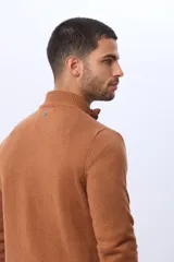 Buzo de punto color beige, con cuello alto y cierre frontal con cremallera y solapa de gamuza con botón. Presenta un tejido texturizado en el cuerpo y mangas lisas.