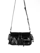 Cartera de hombro negra de charol, con solapa frontal asegurada con hebilla y correa ajustable. Presenta dos bolsillos frontales con cierres y ojales metálicos, además de detalles de cordones con ojales en los laterales. Incluye un dije metálico con las letras 'R' y 'O' entrelazadas.