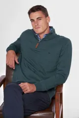 Buzo de tejido fino en hilo de algodón, color rosado, con cuello alto y cierre frontal parcial con detalle en cuero. Presenta puños y ruedo acanalados y un pequeño logo bordado en el pecho.