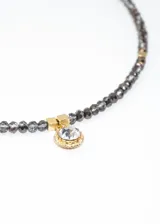 Gargantilla de mostacillas grises con detalles de acero quirúrgico dorado y dije circular con strass.