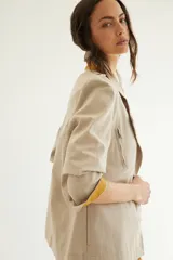 Chaqueta corta de inspiración motoquera color beige, confeccionada en lino fantasía, sin forro, con cierres decorativos, broches de presión y bolsillos delanteros funcionales. Presenta detalle bajo el cuello y en vueltas de mangas en color mostaza y rayas.
