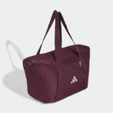 Bolso deportivo Adidas de color bordó, con asas superiores, correa ajustable cruzada y el logo de la marca impreso en blanco en la parte frontal. Cuenta con cierre superior y bolsillo frontal con cremallera.
