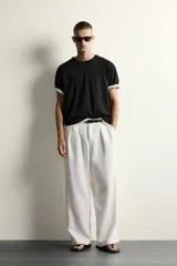 Pantalón relaxed fit de color blanco off-white, confeccionado en tejido con lino. Cuenta con pliegues frontales en la cintura, bolsillos delanteros y cierre frontal con cremallera y botón.