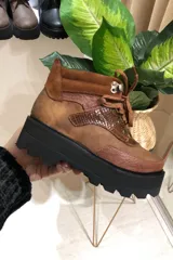Bota acordonada de cuero color marrón con detalles en cuero con textura de reptil y gamuza color marrón claro. Tiene plataforma de goma negra con suela dentada.