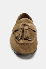 Mocasín de mujer confeccionado en serraje color marrón, con detalle de antifaz y borlas en el empeine. Presenta punta redonda y suela plana.