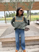 Sweater de tejido de punto color verde oliva, con cuello redondo y detalle de recortes en cuero color camel en la parte frontal. Presenta mangas largas y un corte holgado.