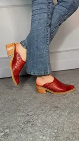 Zuecos Cindy de punta cerrada, confeccionados en cuero rojo con perforaciones artesanales. Poseen un diseño abierto en el talón y taco ancho de madera.