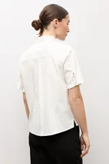Camisa blanca de manga corta con cuello mao y detalles de volados a lo largo de la botonera frontal y en los puños.